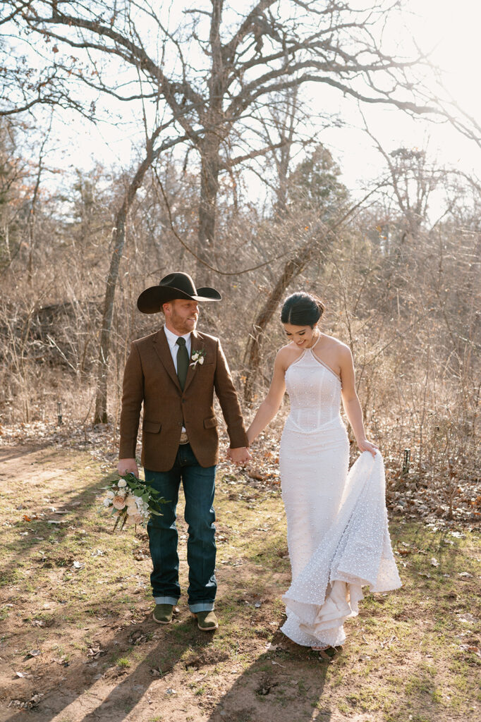 A bride and groom hold hands while taking rustic wedding portraits during their microwedding. 