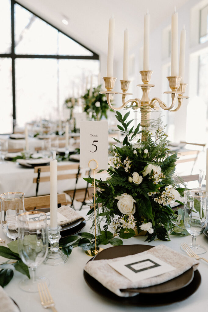 A microwedding tablescape featuring a gold candelabra, taper candles, and a large, rose floral arrangement with greenery. 