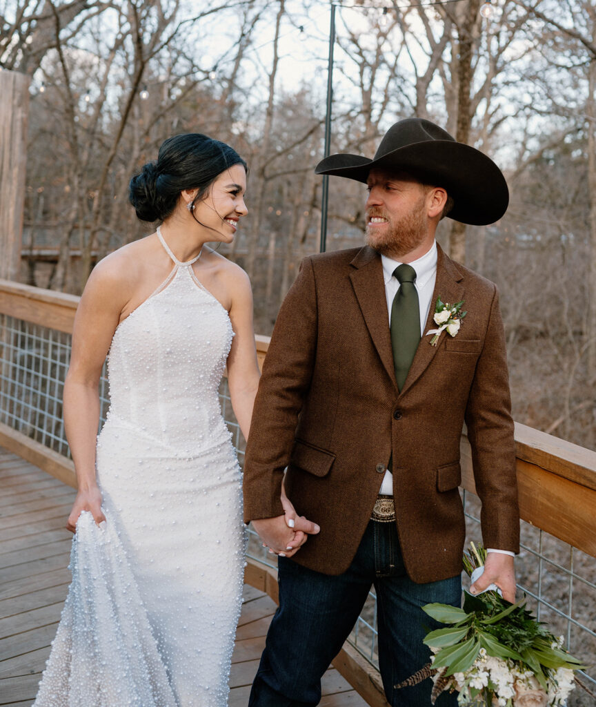 A bride and groom walk along a wooden bridge in a forest during their rustic microwedding. 