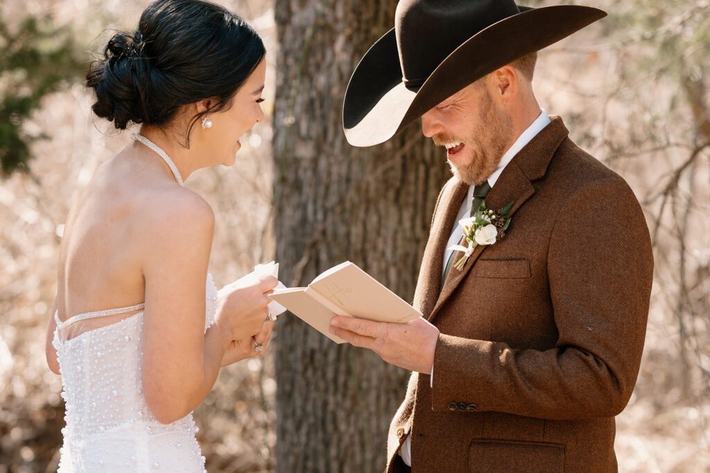 A bride and groom share laughter while reciting written wedding vows during their microwedding ceremony outdoors. 