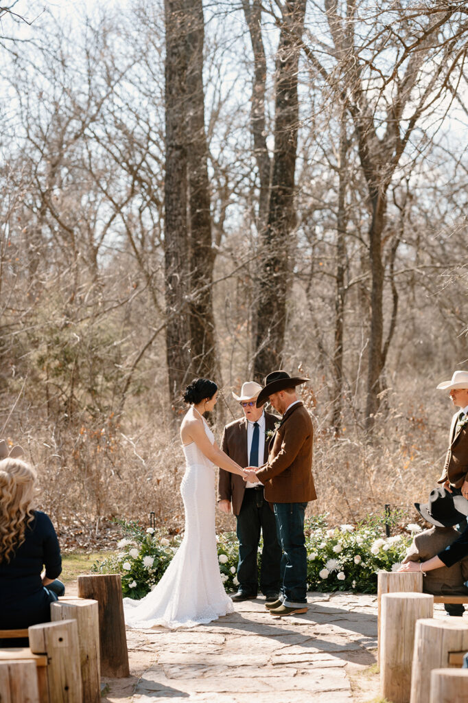 An officiant recites vows during a bride and groom's rustic microwedding ceremony outdoors. 