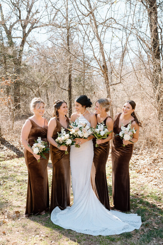 A bride, wearing a long, beaded wedding gown, poses with her bridesmaids, who are all wearing brown velvet bridesmaid dress.