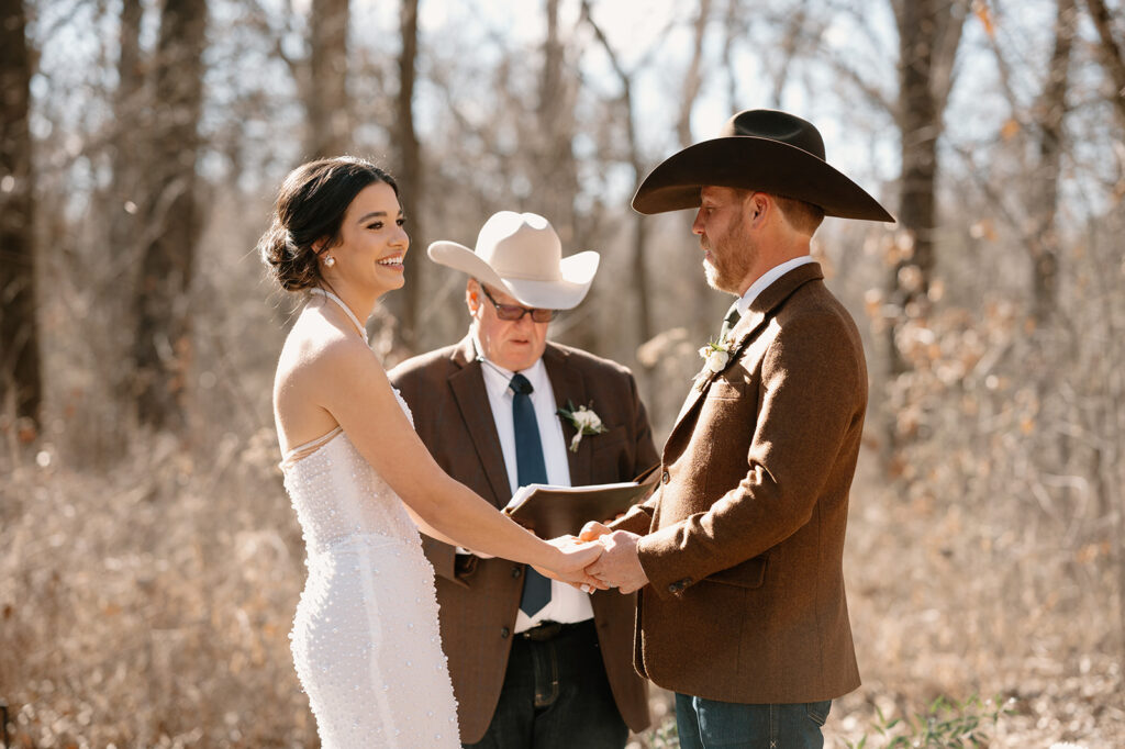 A bride smiles towards microwedding guests during a vow ceremony. 