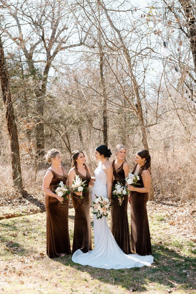 A bridal party, all wearing long, brown velvet bridesmaid dresses, poses for a portrait with a bride. 