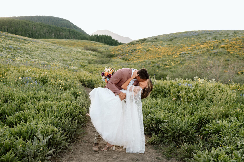 A groom dips his bride on a hiking trail that runs through a wildflower meadow in Crested Butte. 