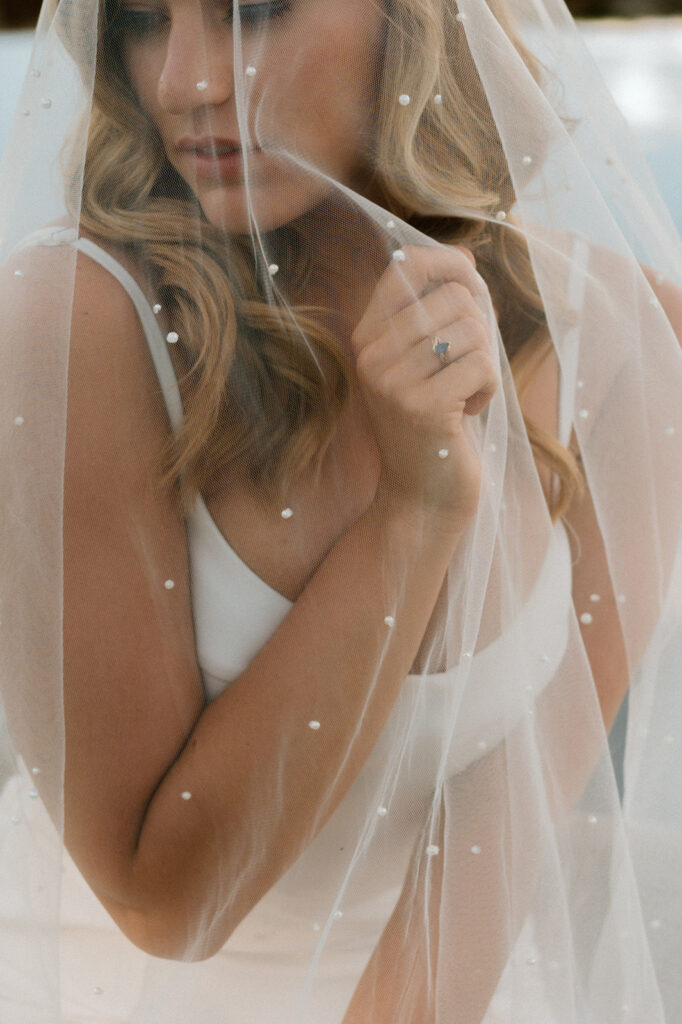 A bride holds her tulle wedding veil with embellishments in front of her face. 