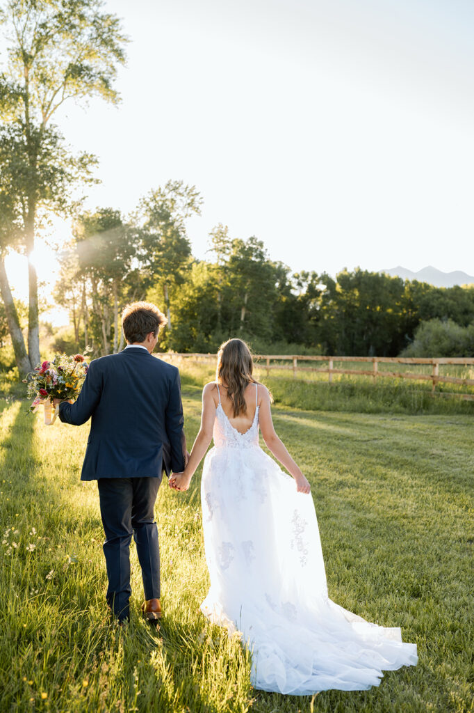 A couple walks while holding hands through a meadow during their intimate wedding at Shaw's River Ranch.