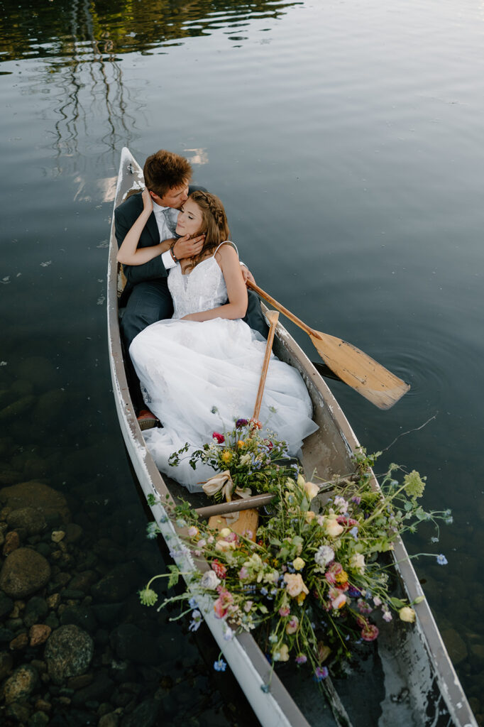 A newlywed couple in wedding attire sit in a row boat during their pond ceremony at Shaw's River Ranch.