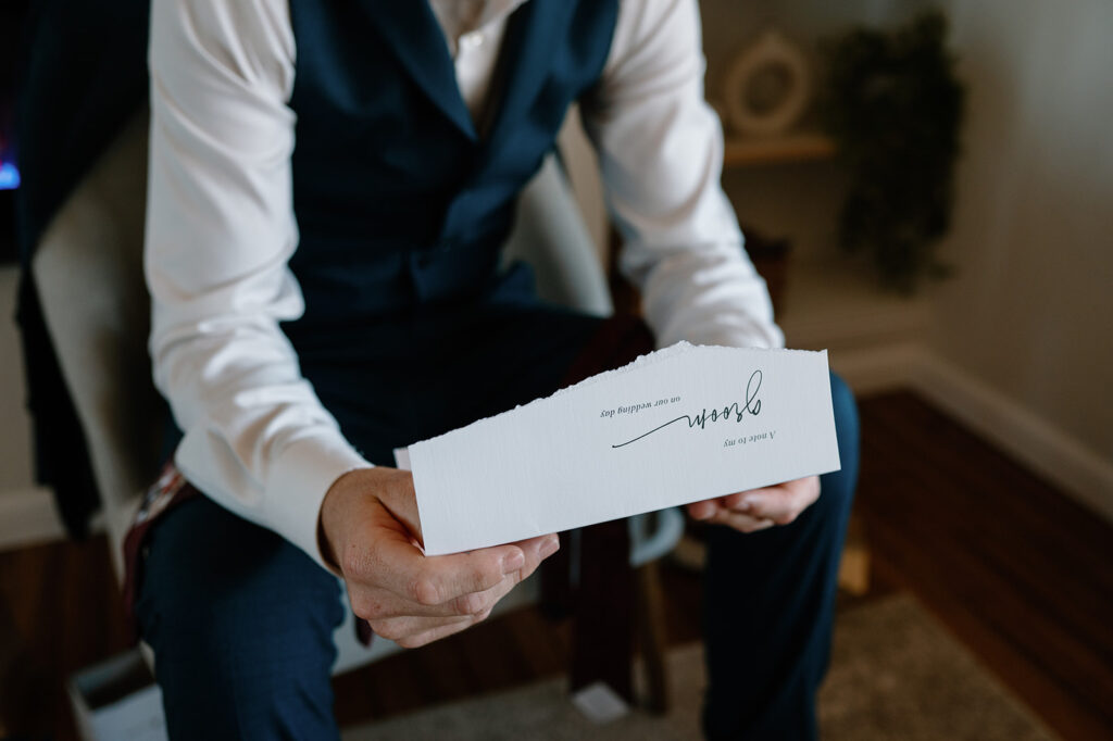 A groom in a navy tux reads a letter addressed to him before his Utah elopement at a Moab Airbnb. 