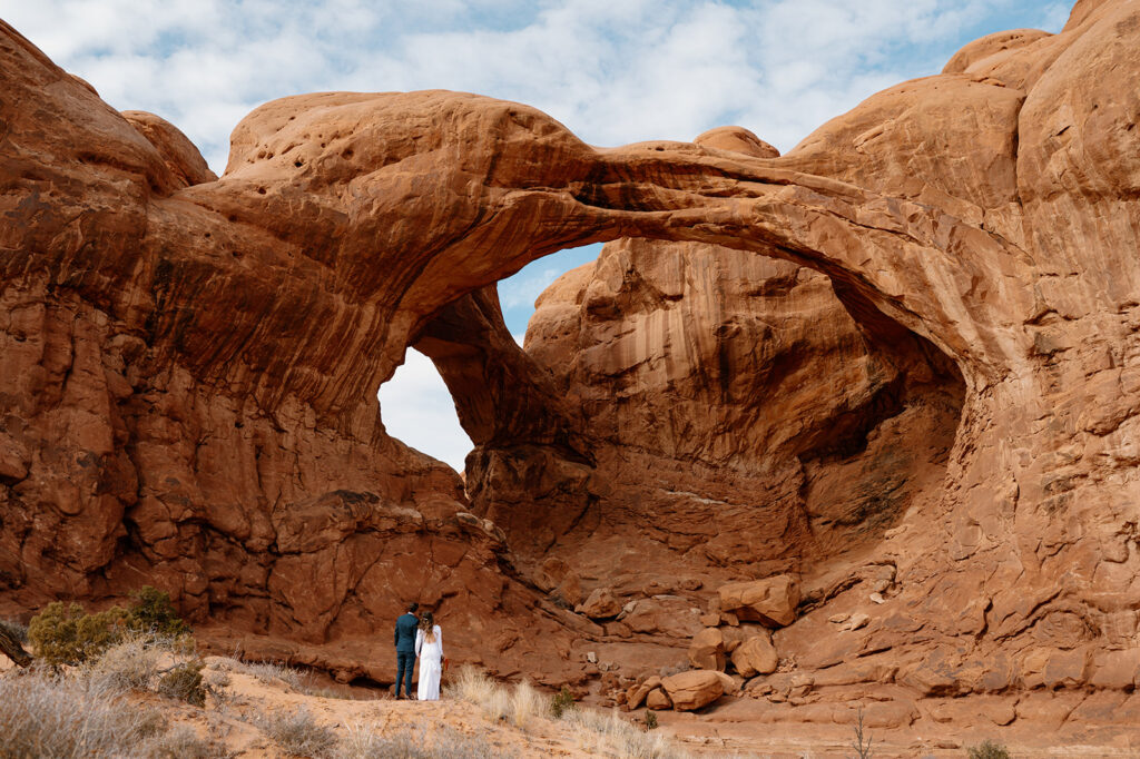 A Utah elopement couple looks up and admires Double Arches in Arches National Park. 