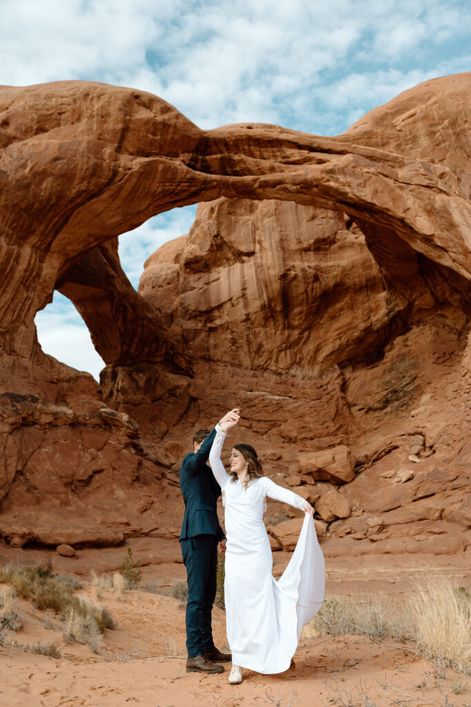 A Moab elopement couple twirls in front of Double Arch in Arches National Park. 