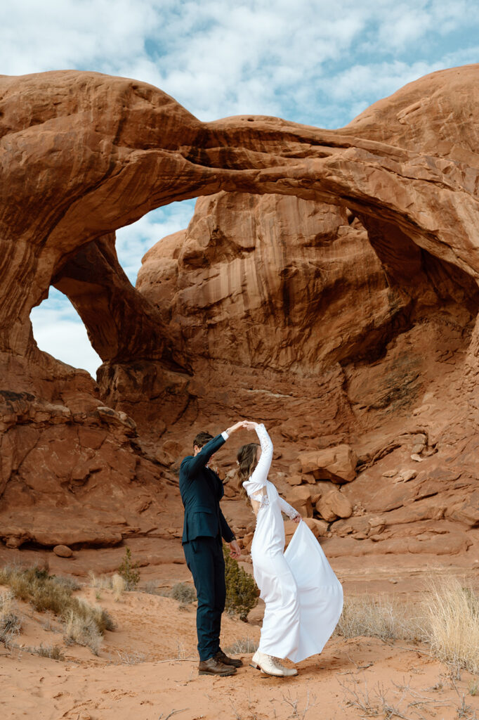 A Moab elopement couple dances in front of Double Arch in Arches National Park. 