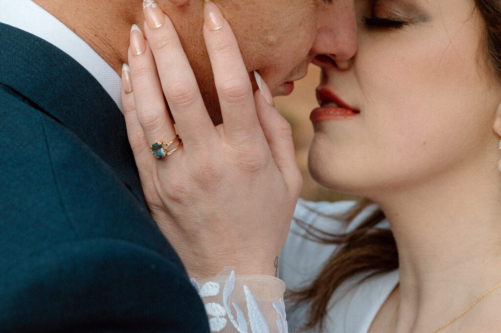 A bride, wearing a gold wedding ring, holds her grooms face during their desert elopement in Moab. 