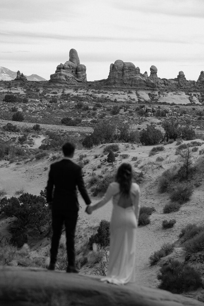 A Utah elopement couple holds hands while admiring the red rock formations of the Moab desert. 