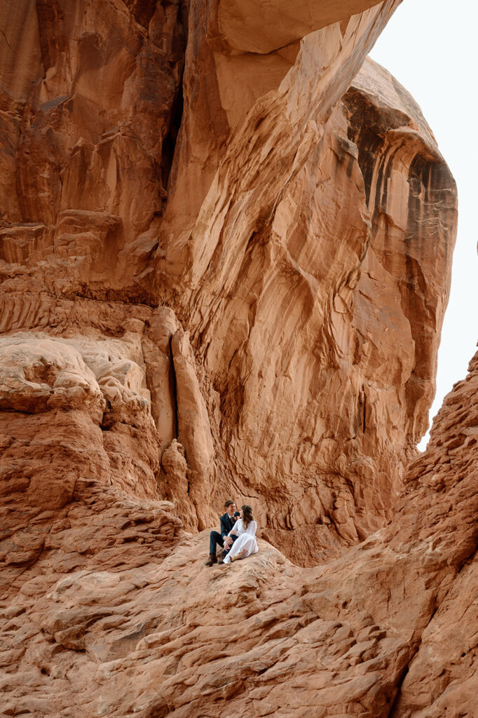 A couple sits beneath a park in Arches National Park during their adventure elopement in Utah. 