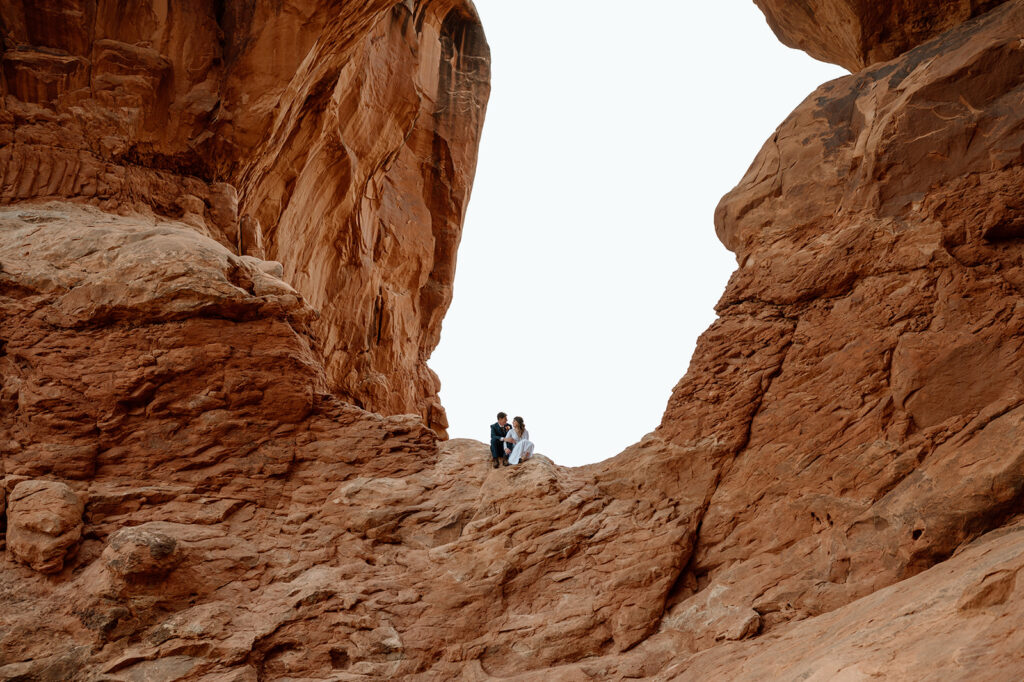 A couple sits in an arch in Arches National Park during their desert elopement in Moab. 