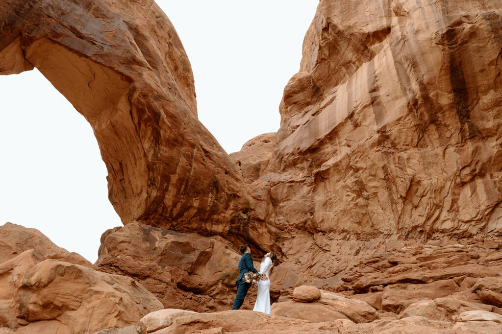 A Moab elopement couple looks up and admires Double Arch in Arches National Park. 