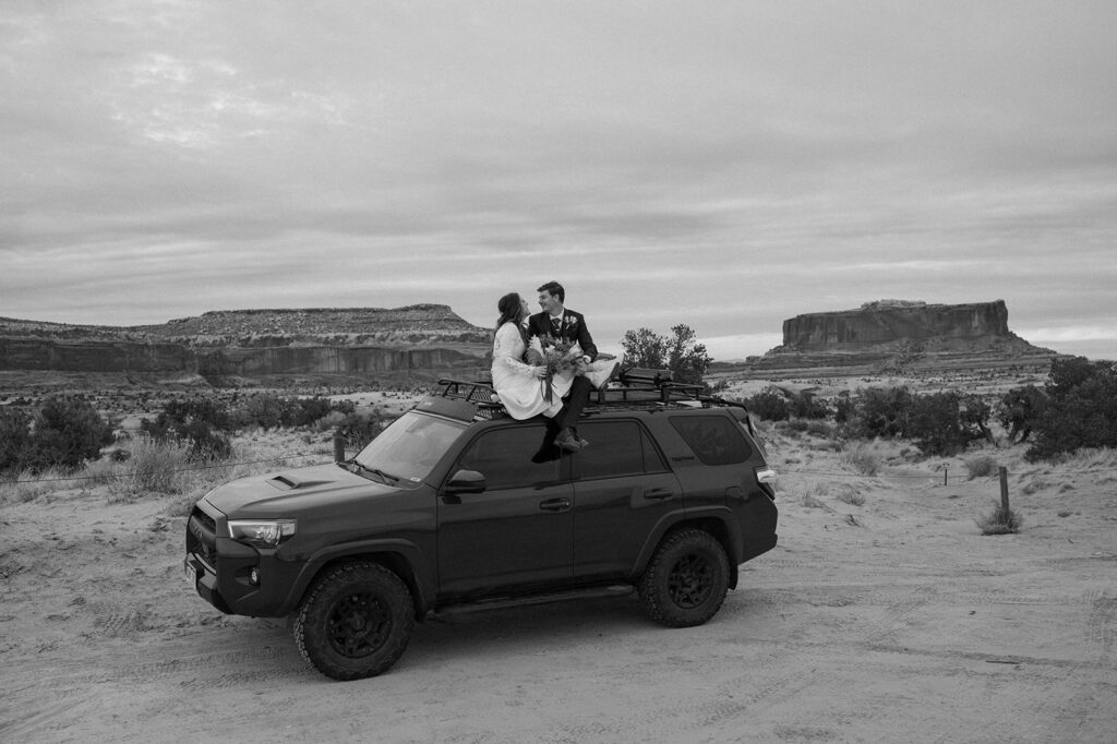 A Utah elopement couple sits atop a Toyota SUV after off-roading in Moab. 