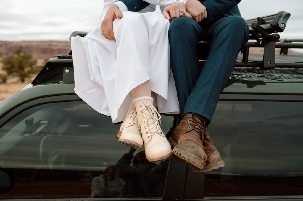 A couple's sits atop a 4x4 vehicle in Moab and show off their hiking shoes worn for their Utah elopement. 