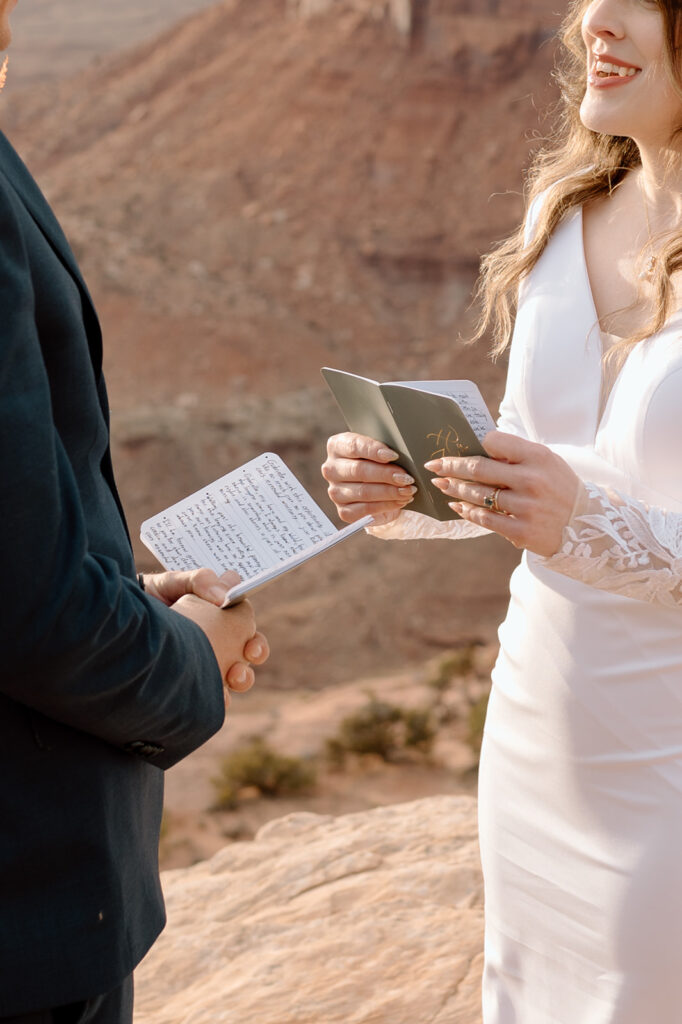 An Utah elopement couple holds green vow books during their intimate ceremony at Grand View Point Overlook in Canyonlands. 