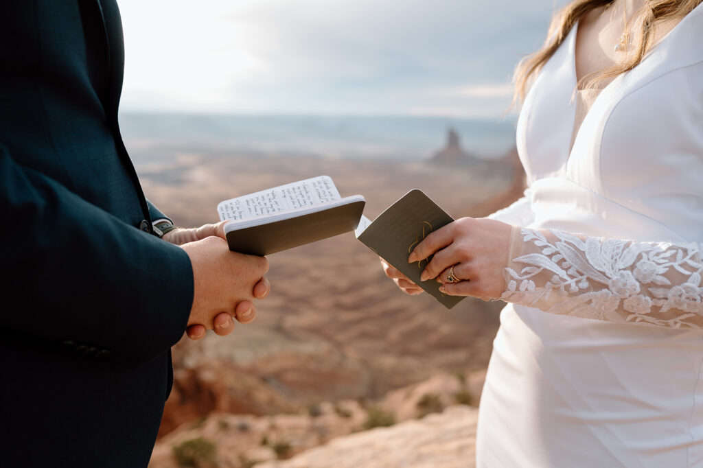 An National Park elopement couple holds green vow books during their intimate ceremony at Grand View Point Overlook in Canyonlands. 