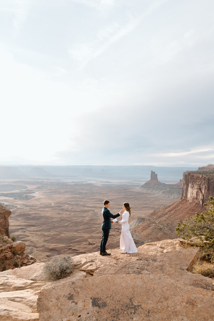 A groom holds his brides face at they recites vows at Grand View Point Overlook during their Canyonlands elopement in Moab. 