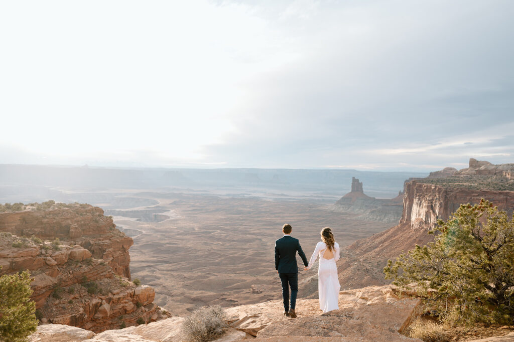 A couple holds hands and looks out onto Canyonlands National Park at Sunset during their Utah elopement.