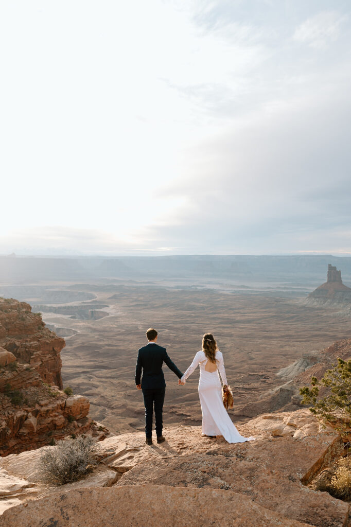 A couple holds hands while looking out onto Canyonlands National Park in Moab during their Sunset desert elopement.