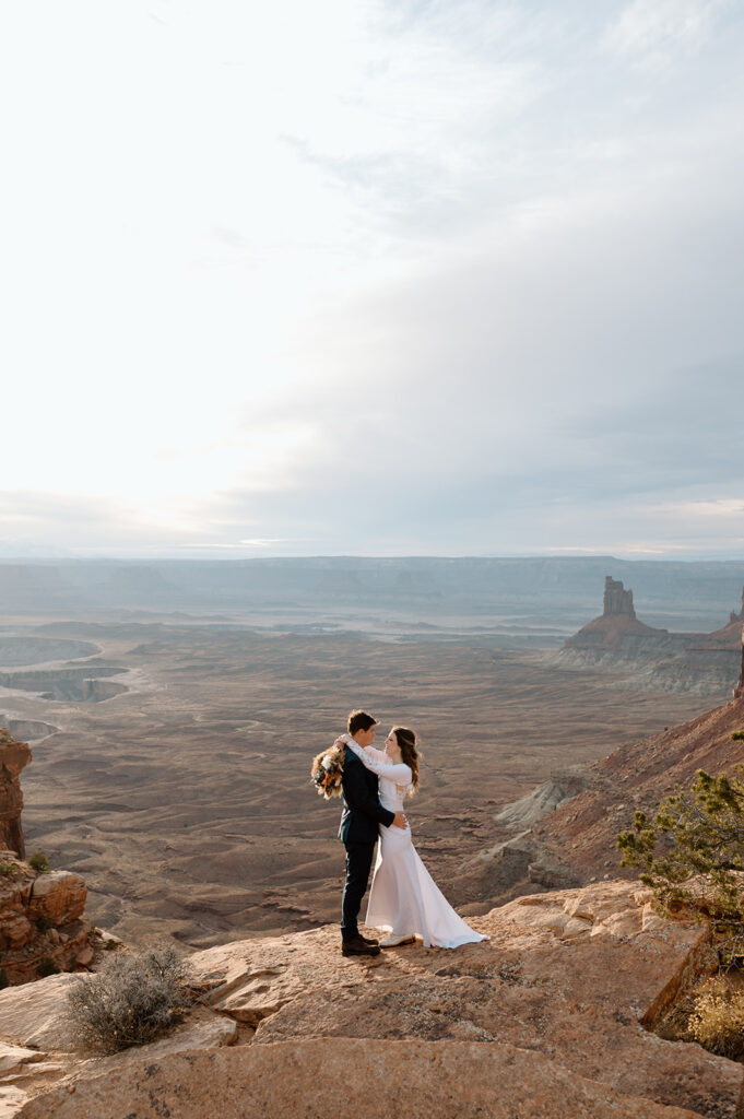 A couple embraces while looking out onto Canyonlands National Park in Moab during their Sunset desert elopement.