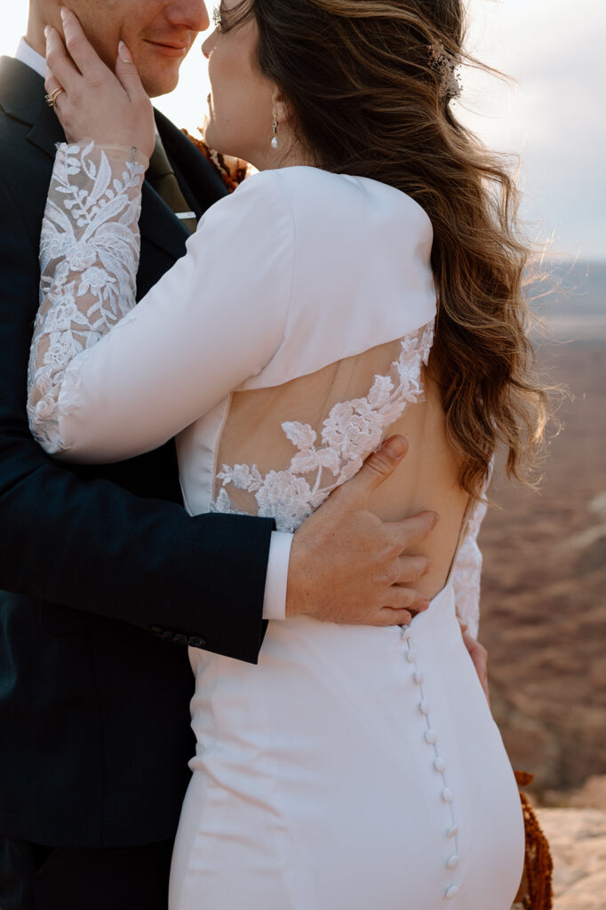 A Moab elopement couple embraces on a cliffside overlooking a desert canyon in Utah.