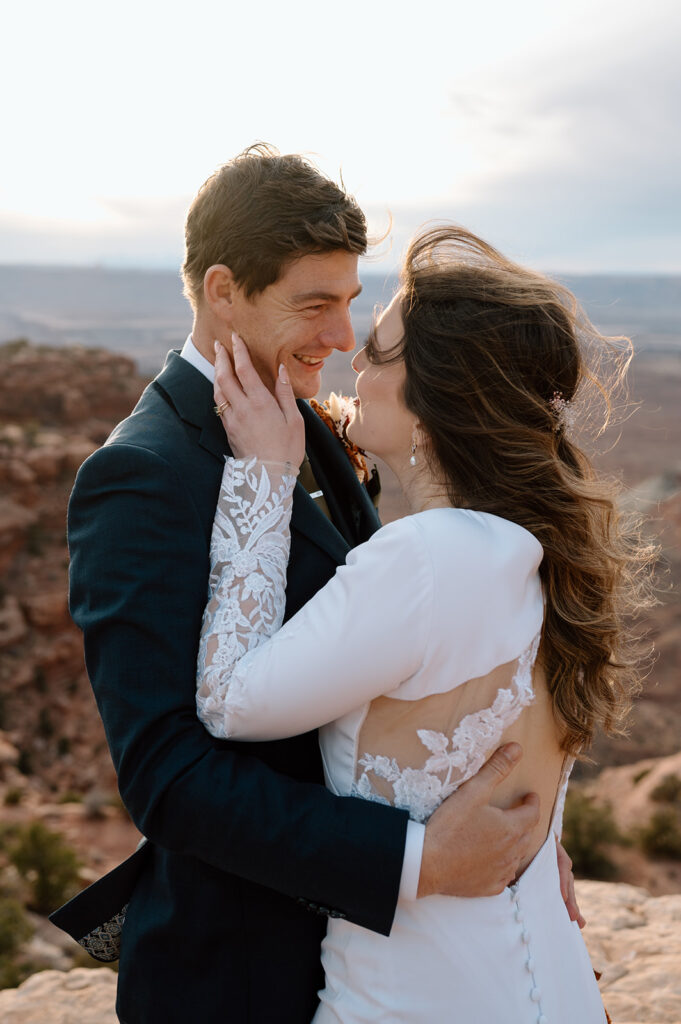 A bride holds her grooms face during their Utah elopement on a Moab overlook. 