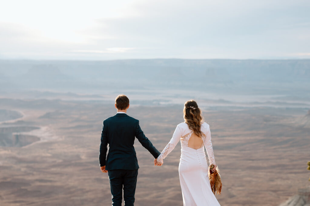 A Utah couple holds hands while standing on an overlook in Canyonlands National Park. 