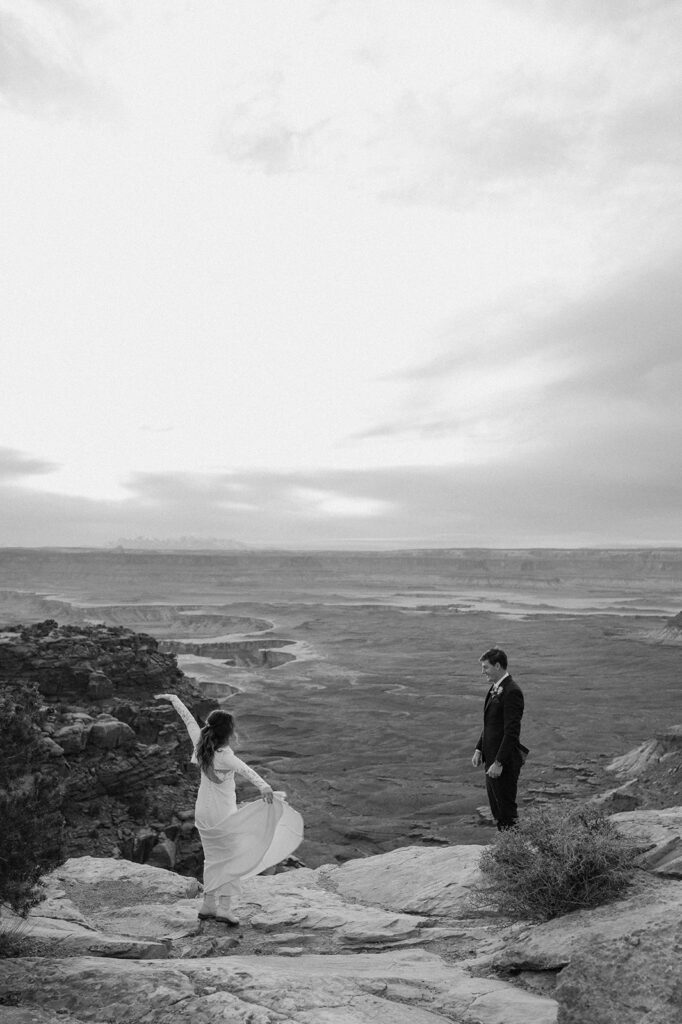 A bride twirls while her groom watches in admiration on an overlook in Canyonlands National Park. 