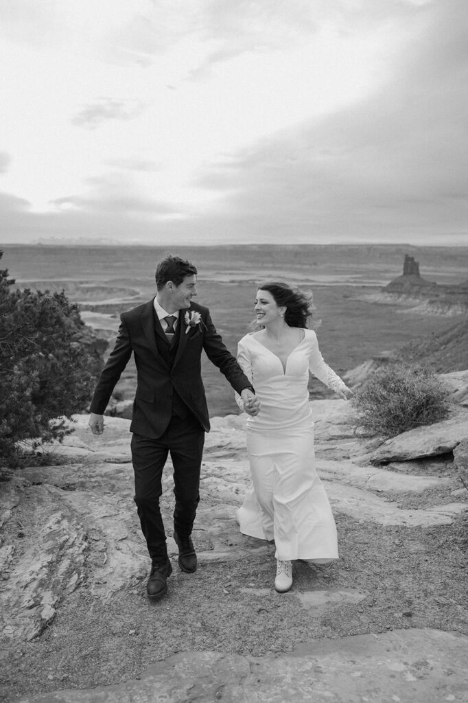 A Moab elopement couple walks along an overlook in Canyonlands National Park wearing wedding attire. 