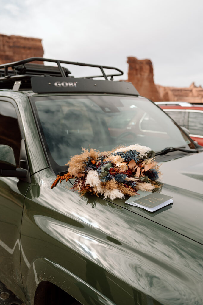 A dried floral bouquet sits atop a Toyota SUV's hood, along with green vow books. 