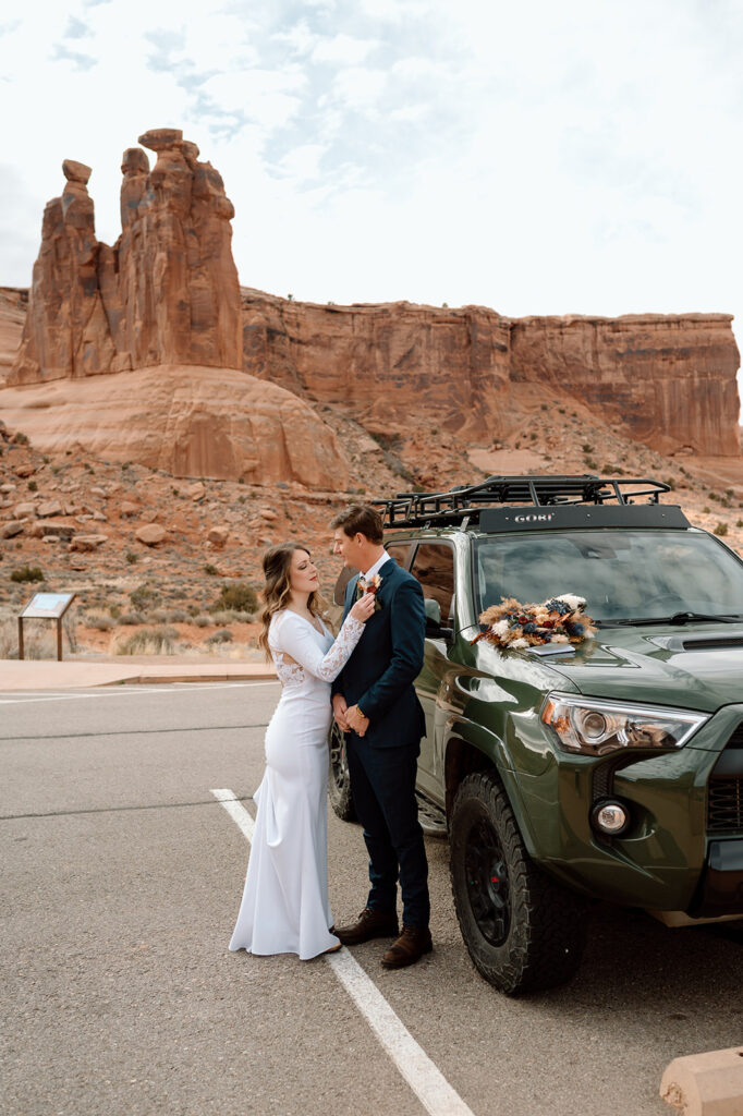 A Utah elopement couple stands near a Toyota SUV while they get ready for their desert vow ceremony in Moab. 