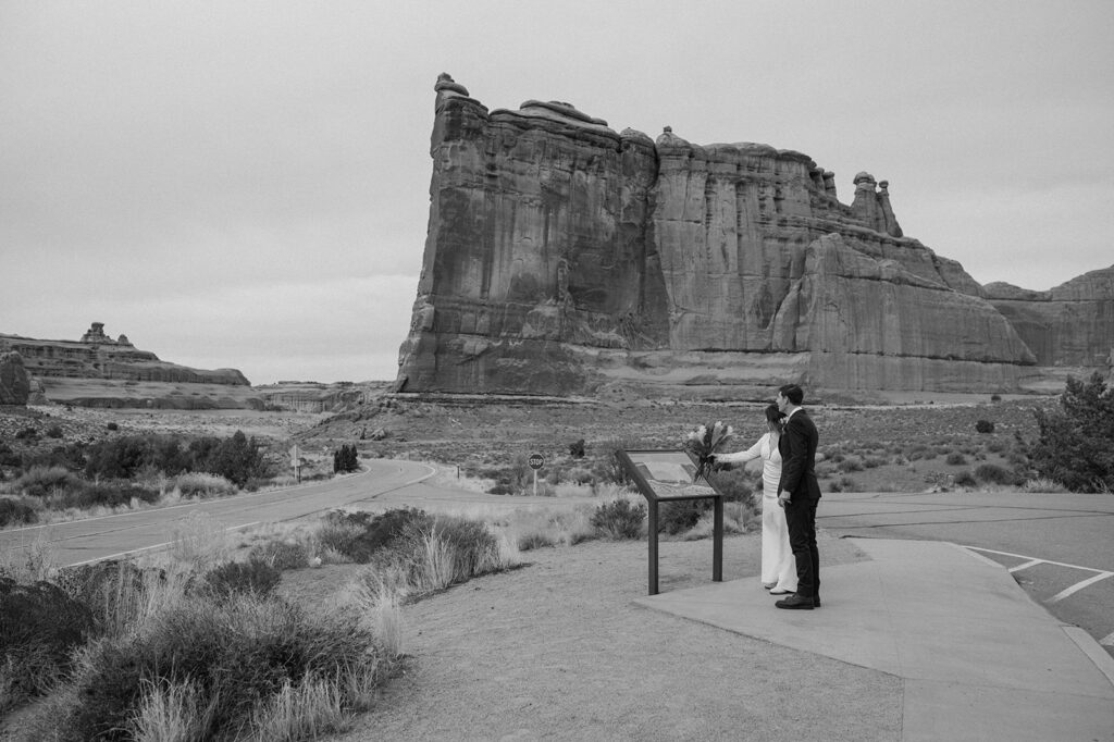 A Moab elopement couple looks at a hiking trail map in Arches National Park before their desert elopement. 