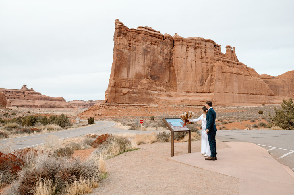 A Utah elopement couple looks at a map of Arches National Park. 