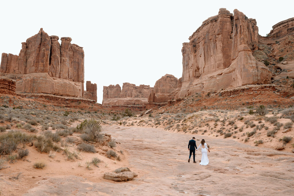 A Moab elopement couple walks hand in hand in Arches National Park. 