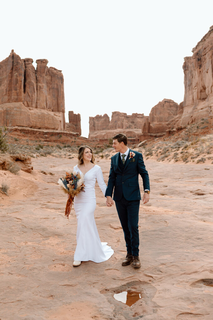 A couple holds hands on a path in Arches National Park during their adventure elopement in Moab, Utah. 