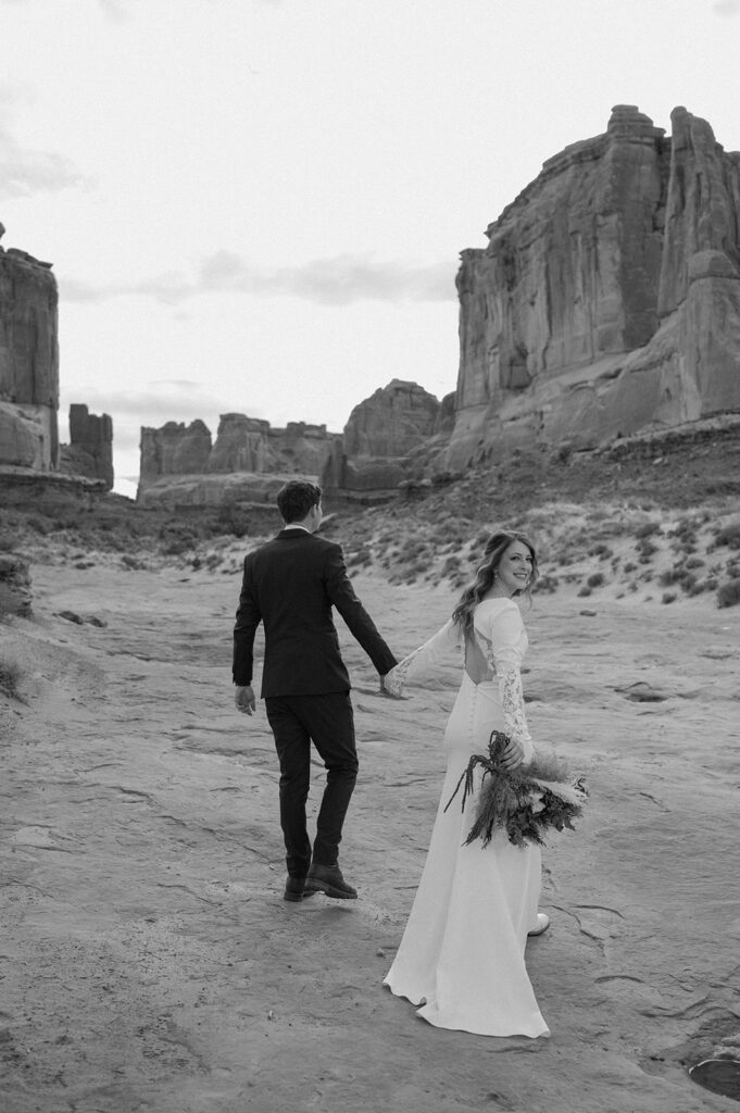 A Utah elopement couple walks along red rocks in Arches National Park. 