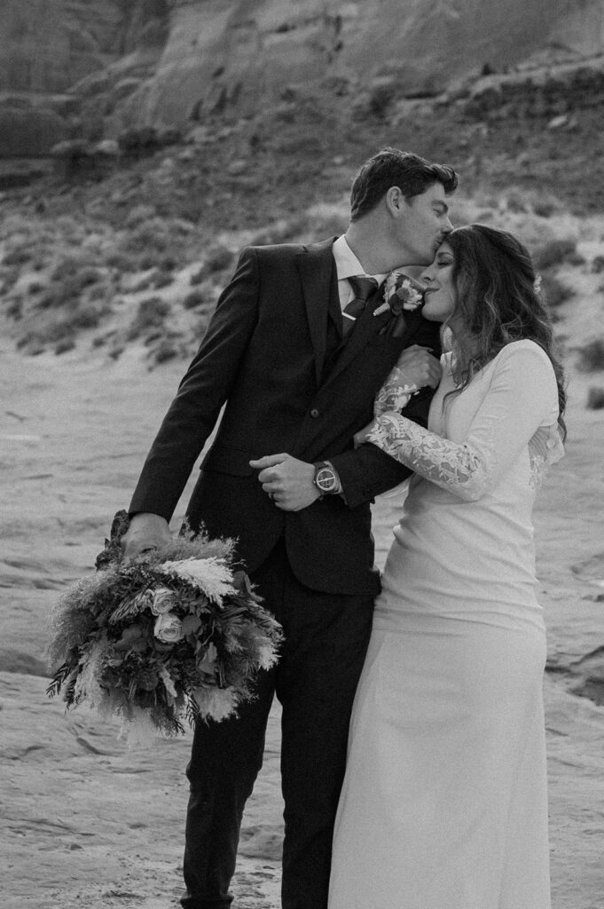 A groom kisses his bride's forehead while holding her dried floral bouquet during their Utah elopement. 