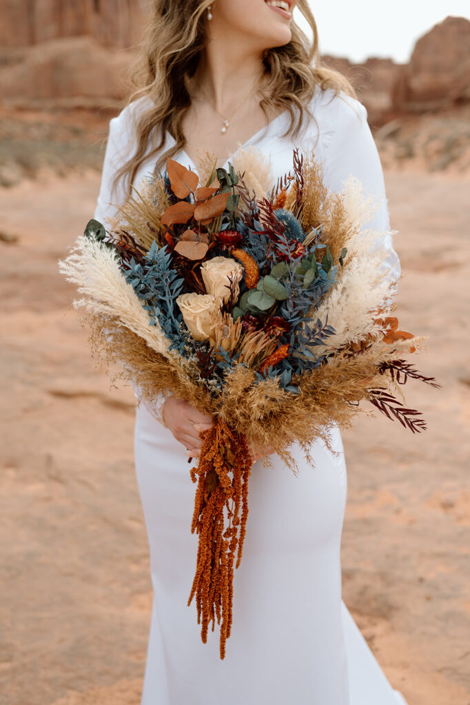 A woman wearing a long, white wedding dress holds a large, dried bridal bouquet during her Utah elopement. 